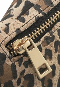 Leopardmønstret ruskind med en sort lynlås og guldhardware, der har et rektangulært lynlås-træk med udskæringsdetalje.