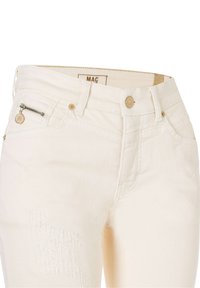 Jean en denim écru avec fermeture par bouton, poche zippée sur le devant gauche, passants pour ceinture et légères déchirures sur la cuisse gauche.