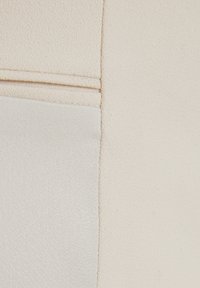 Beige kangasta, jossa on sileä pinta ja hienovarainen rakenne, sekä kaksi erilaista osaa. Saumassa näkyvät ompeleet.
