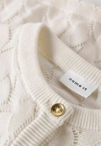 Pull en tricot crème avec des motifs de cœurs texturés, col à côtes, bouton doré et étiquette avec l'inscription "name it".