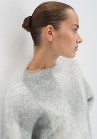 Helles graues und weißes flauschiges Sweatshirt mit rundem Ausschnitt und weicher Textur, das sanft über die Schultern fällt und einen lässigen Schnitt aufweist.
