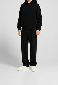 Svart bomullshoodie med kenguruficka, kombinerad med svarta vida jeans och vita sneakers, alla med en enkel, monokrom design.