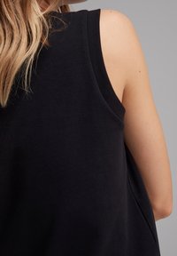 Top senza maniche nero realizzato in tessuto morbido, con una vestibilità comoda, ampie aperture per le braccia e una superficie liscia e opaca.