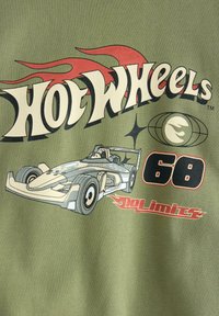 Un tessuto verde oliva presenta un design grafico con il testo "Hot Wheels", un'illustrazione di un'auto da corsa e il testo “68” affiancato da "No Limits."