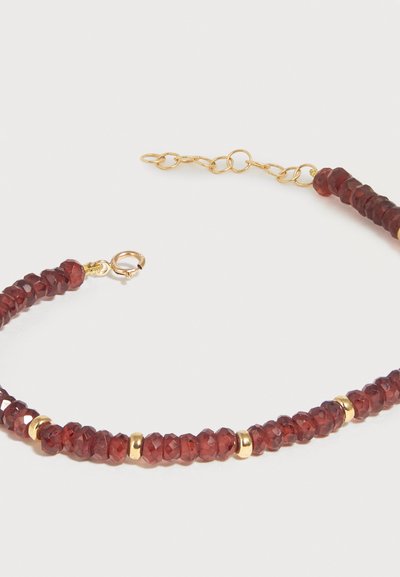 Κολιέ από κόκκινα πολύγωνα πετράδια με χρυσά διαχωριστικά χάντρες και κούμπωμα αλυσίδας με ρυθμιζόμενους κρίκους σε λευκό φόντο.