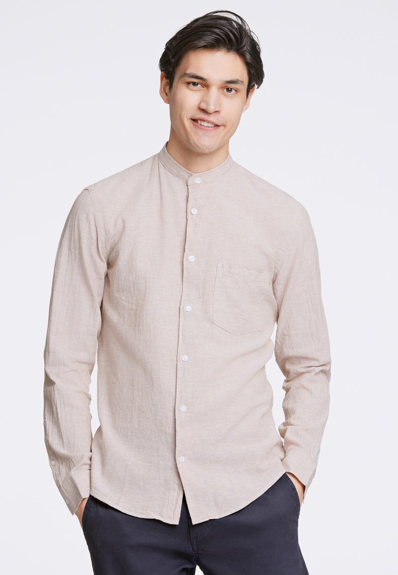 Camicia a maniche lunghe color beige chiaro con colletto alla mandarino, chiusura a bottoni e una tasca sul petto, realizzata in un tessuto testurizzato.
