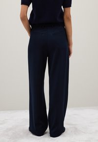 Navy wijde broek gemaakt van gladde stof, met twee achterzakken. Het ontwerp heeft een strakke, op maat gemaakte silhouette.