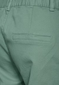 Pantalons en coton vert clair avec une poche arrière dotée de coutures soignées et d'une surface côtelée texturée. Taille élastique visible.