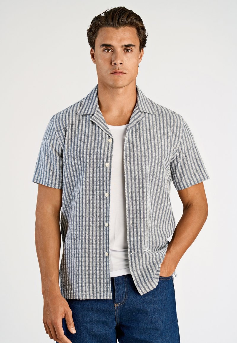 Koszula z krótkim rękawem zapinana na guziki, w pionowe niebiesko-białe paski, wykonana z teksturowanej tkaniny, z kołnierzem typu rozłożystego i dwoma przednimi kieszeniami.