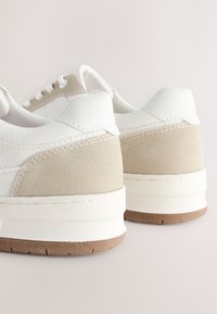 Hvide og beige sneakers med en tekstureret læderfinish, ruskindsdetaljer og en tyk hvid sål. Har snørebånd og en polstret krave.