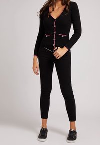 Czarny prążkowany kardigan z różowym wykończeniem, z przodu zapinany na guziki, z dwoma kieszeniami. Noszony z czarnymi obcisłymi dżinsami i czarnymi tenisówkami.