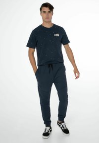 Navyfarbener Baumwoll-T-Shirt mit bunten Spritzern und Logo auf der Brust, kombiniert mit passenden Jogginghosen mit elastischem Bund und seitlichen Taschen.