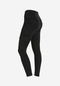 Leggings neri in denim con vita alta, design aderente, tasca cargo laterale e texture liscia. Presentano cuciture rinforzate e una silhouette elegante.