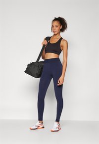 Top sportivo nero, leggings blu navy, scarpe da corsa grigie e arancioni, e una borsa da palestra nera; tessuto morbido, design aderente e vita elastica.