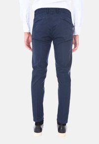 Chinos blu navy con vestibilità slim, in tessuto di cotone, due tasche posteriori e cerniere metalliche. Indossati con scarpe nere, che offrono un aspetto pulito e su misura.