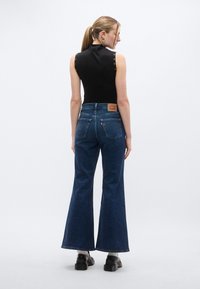 Μαύρο αμάνικο τοπ με κουμπώματα στους ώμους, συνδυασμένο με μπλε τζιν παντελόνι καμπάνα που διαθέτει δερμάτινο λογότυπο και δύο τσέπες πίσω.