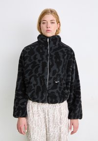 Črna puhasta jakna z visokim ovratnikom, zadrgo in vzorcem živali; na sprednjem levem delu ima majhen bel Nike logotip.