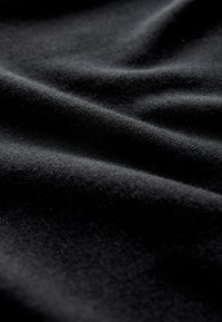 Primo piano di tessuto nero morbido con trama visibile e pieghe delicate che creano ombre e luci morbide.