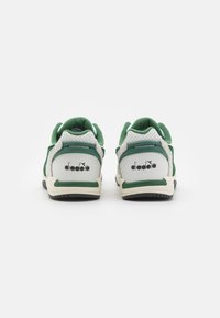 White and green sneakers with a textured suede finish, perforated details, and a logo at the heel. Features a black rubber sole.