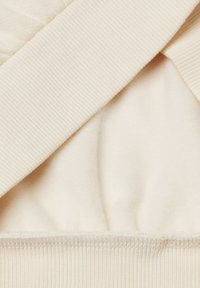 Tessuto beige con texture a costine, caratterizzato da un rivestimento interno liscio. Il design include un aspetto stratificato con cuciture ben visibili.
