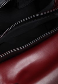 Borsa aperta che mostra due scomparti, uno in tessuto nero e uno in pelle bordeaux, con texture lisce e colori contrastanti.