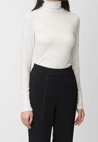Witte lange mouw turtleneck top, gemaakt van zachte stof, gecombineerd met zwarte, elastische taillebroek. Opvallende gladde textuur en aansluitend ontwerp.