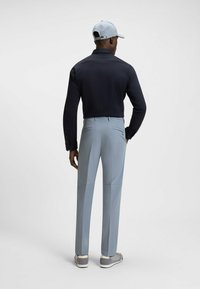 Men's outfit featuring a dark long-sleeve polo and light gray pants. The polo has a collar and button accents; the pants feature back pockets.