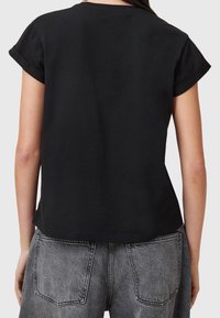 T-shirt en coton noir avec des manches courtes retroussées, un ourlet droit et une coupe décontractée. Le dos présente une texture lisse et unie sans graphiques.