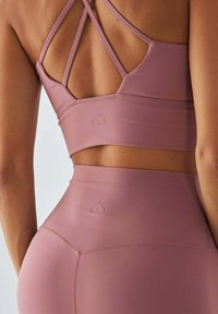 Jasnoróżowy sportowy biustonosz i legginsy z wysokim stanem, z krzyżującym się zapięciem na plecach oraz subtelnym logo w kształcie serca na pasie.