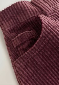Burgundy corduroypuuvilla, jossa on pystysuora ribbitekstuuri; siinä on leveä, rakenteellinen vyötärö ja sivutasku. Pehmeä ja lämmin ulkonäkö.