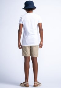 Camiseta blanca, pantalones cortos beige y un sombrero de cubo azul marino. La camiseta tiene un corte estándar; los pantalones cortos son ligeros y terminan por encima de las rodillas.