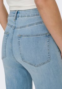 Light blue denim jeans with a high waist, featuring two back pockets, subtle stitching, and a smooth texture.