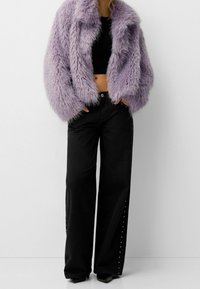 Lilla kunstpelsjakke med en cropped design og brede, fluffy ærmer, parret med sorte jeans med høj talje og nittede detaljer i siderne.