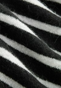 Schwarz-weiß gestreifter Stoff, weiche Textur mit sichtbaren Fasern, in Falten angeordnet, die die kontrastierenden Farben und Muster hervorheben.