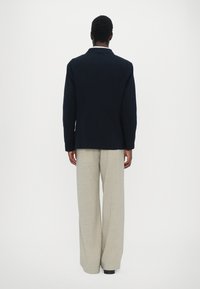 Navy jacket with a notched collar and long sleeves, paired with light beige wide-leg trousers. Smooth fabric and relaxed fit.