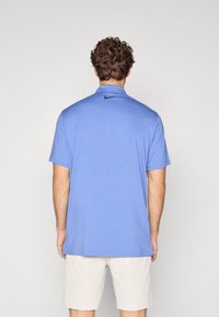 Nike kortærmet polo skjorte i lys blå, med et struktureret stof, krave og et sort logo på den øverste del af ryggen.