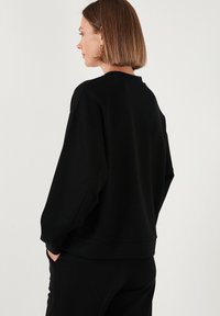 Felpa nera over size con spalle abbassate, polsini a costine e colletto rotondo. Realizzata in un tessuto morbido con una superficie liscia.
