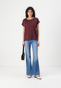 Tricou scurt burgundy cu guler rotund, asortat cu blugi evazați de culoare bleu deschis. O geantă neagră și balerini bej completează ținuta.