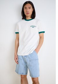 Hvit bomulls t-skjorte med grønn krage og ermeaksenter, med en liten logo på brystet. Kombinert med lyseblå denimshorts.