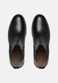 Bottines en cuir noir avec des panneaux latéraux en élastique, bout rond, texture lisse et doublure intérieure beige clair. Design minimaliste.