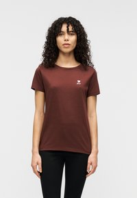 Καφέ βαμβακερό μπλουζάκι με κοντά μανίκια, στρογγυλή λαιμόκοψη και λευκό λογότυπο σε σχήμα καρδιάς στο στήθος. Λείος υφής με άνετη εφαρμογή.