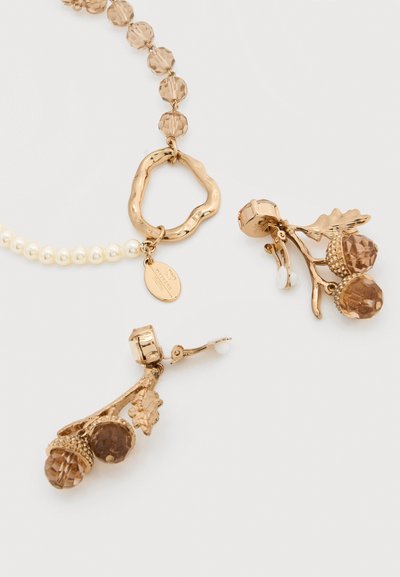 Κολιέ σε χρυσό τόνο με ακανόνιστο ανοιχτό κρίκο και χάντρες, σετ με αντίστοιχα σκουλαρίκια με βιδωτό κούμπωμα που διαθέτουν καρύδια σε σχήμα βελανιδιάς με καφέ κρύσταλλα και φύλλα.