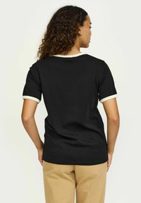 T-shirt noir avec des manches courtes, bord crème contrastant au col et aux manches. Tissu en coton lisse, coupe décontractée.