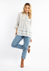 Blusa leggera a maniche lunghe con bottoni, a righe blu e bianche, abbinata a jeans blu rilassati e stivaletti marroni.