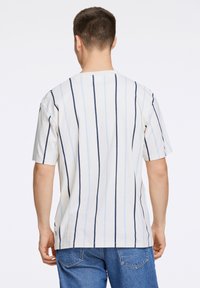 Korte mouwen, ronde hals T-shirt in lichtbeige met marineblauwe en lichtblauwe verticale strepen. Zachte katoenen stof met een ontspannen pasvorm.