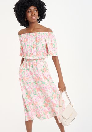 Blumen-Off-Shoulder-Kleid in Rosa, Orange und Grün mit gerüschtem Taillenbund und fließendem Rock. Kombiniert mit einer handlichen hellen Tasche.