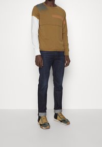 Camisa de manga larga en bloques de colores marrón y blanco, combinada con jeans azul oscuro y zapatillas multicolores con textura de ante.