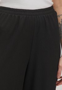 Schwarze, strukturierte Hosen mit einem elastischen Bund, die ein dezentes Knittermuster und eine lockere Passform aufweisen.