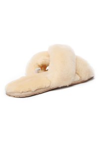 Fuzzy, cream-colored slippers with a cross-band design, soft texture, and a flat, rubberized sole for indoor use. Light and cozy appearance.