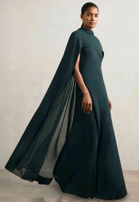 Bodenlanger, dunkelgrüner Abendkleid mit schlankem Design, das mit einer capeartigen Überlagerung und transparenten Einsätzen versehen ist, gefertigt aus glattem Stoff.